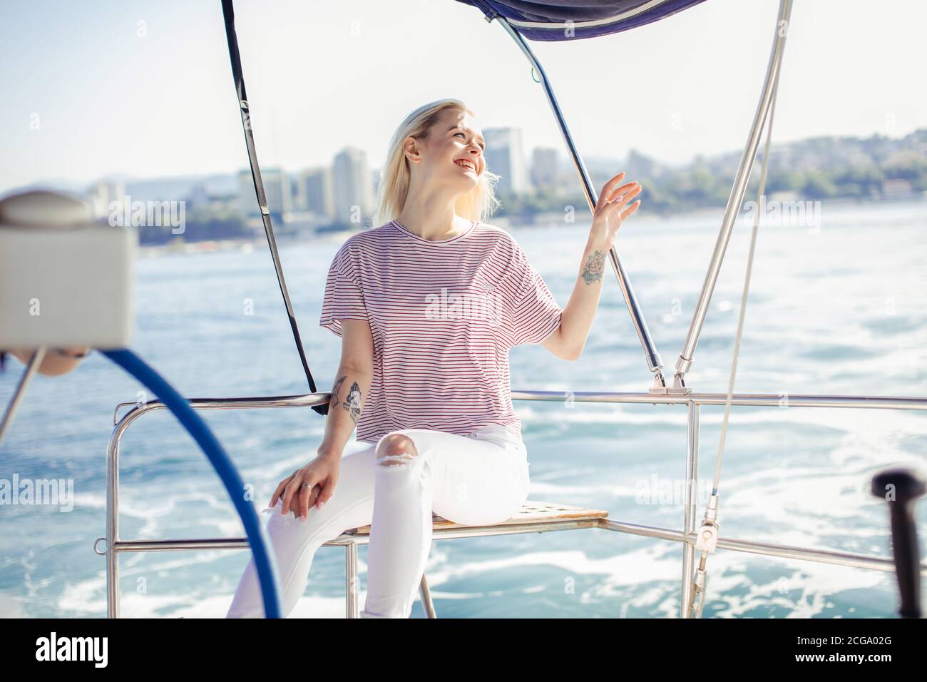 Blonde belle femme sur yacht blanc dans un thème nautique. Blouse à rayures et cheveux blonds. Tenue d'été pour une croisière maritime sur la côte de la mer Banque D'Images