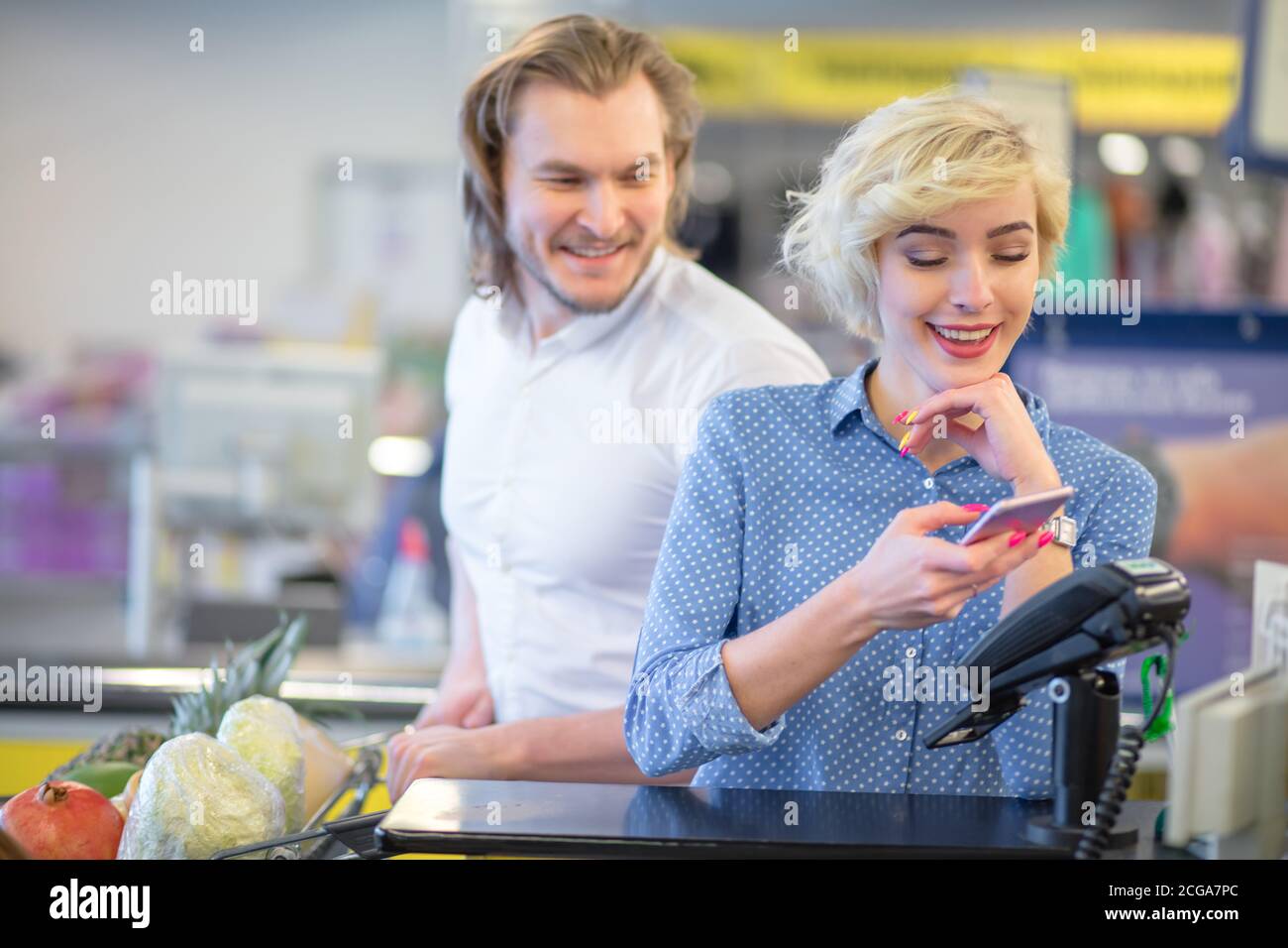 Jeune couple qui fait des achats dans le centre commercial de la ville, blonde jolie femme montre ses coupons à la caisse et obtient une réduction tout en payant avec une carte de crédit! Banque D'Images