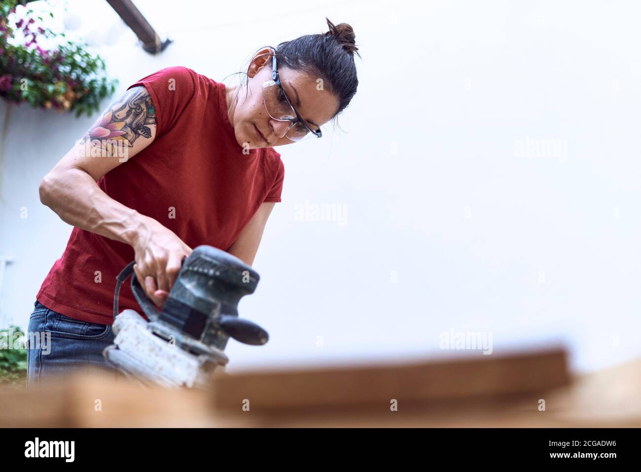 Jeune femme à polir une planche en bois avec une ponceuse à moteur. Concept du travail des femmes Banque D'Images