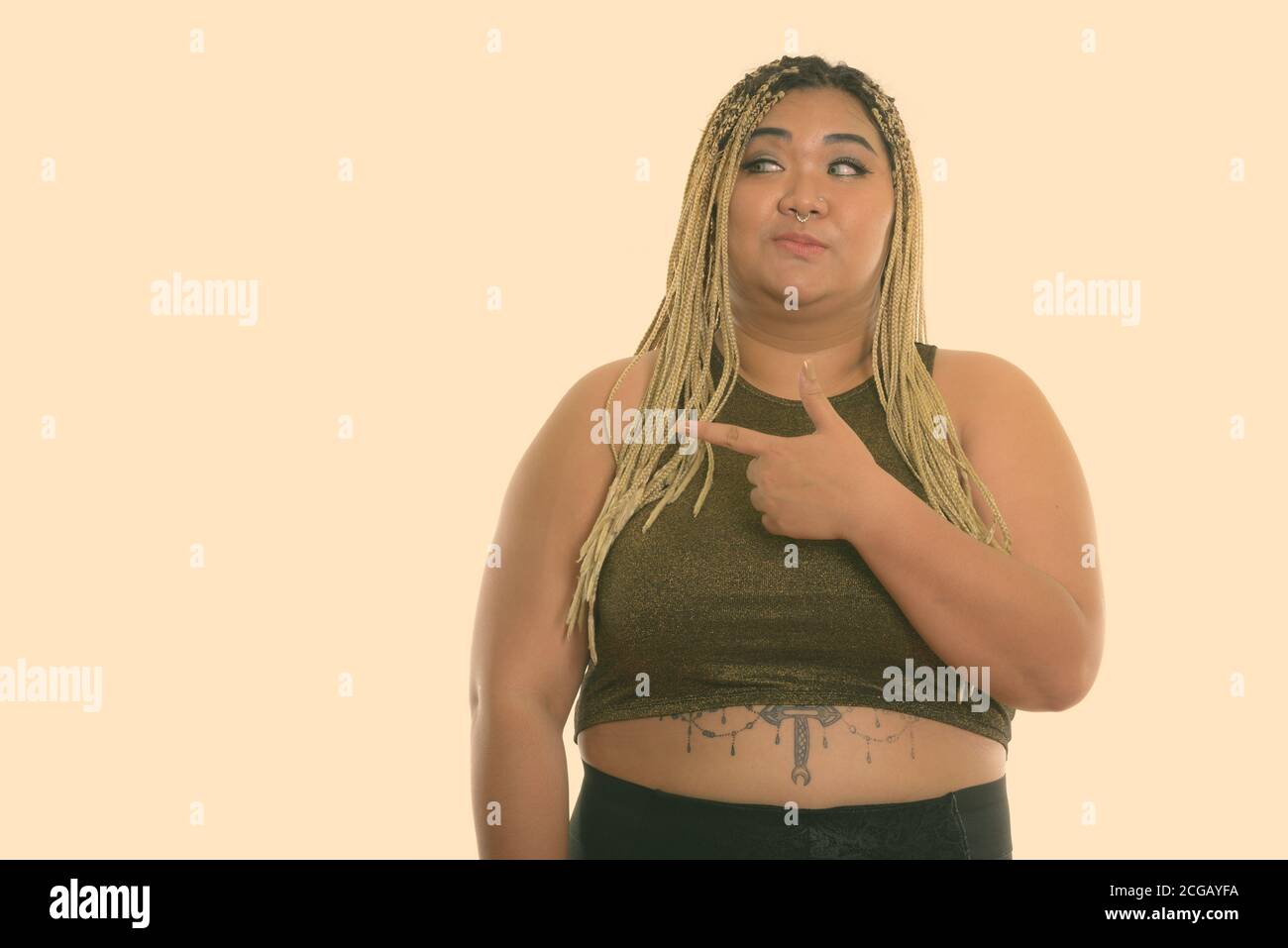 Studio shot of young Asian woman looking fat et montre de l'index sur le côté Banque D'Images