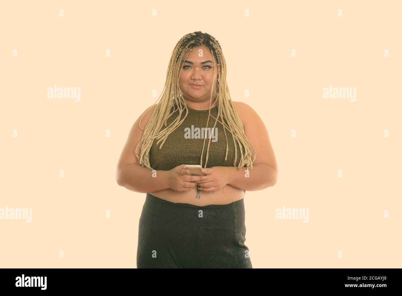 Studio shot of young fat Asian woman holding mobile phone Banque D'Images