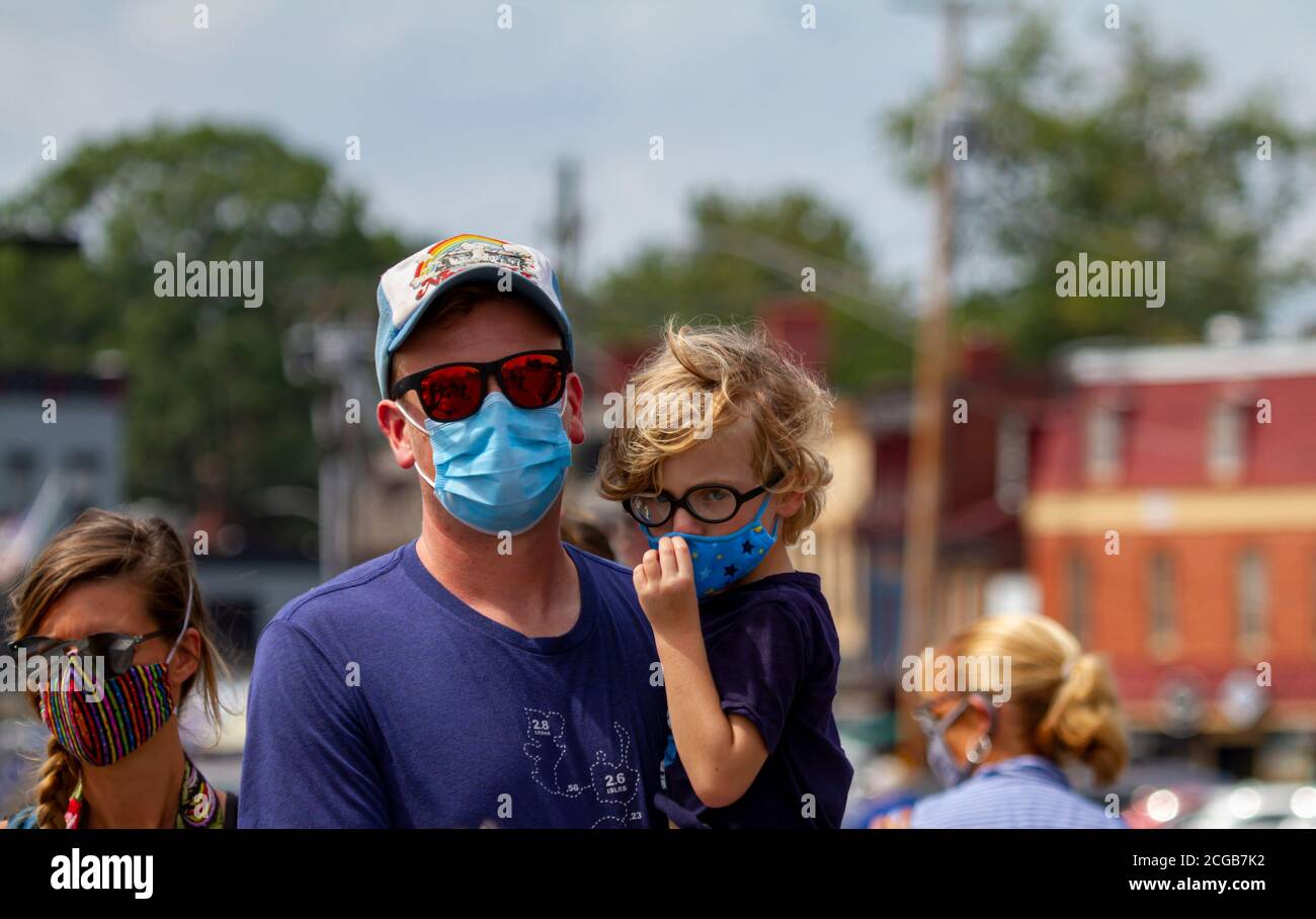 Annapolis, MD, Etats-Unis 08/21/2020: Une famille caucasienne portant des masques pour le visage en raison de COVID-19 marche sur le quai de la ville par une journée ensoleillée. Le père porte sa bl Banque D'Images