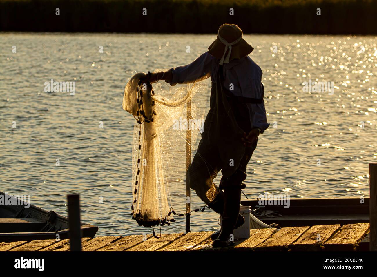 Un pêcheur portant une combinaison, des bottes en plastique et un chapeau de seau prépare son filet de fonte avant de le jeter dans la baie de Chesapeake au coucher du soleil. Il est activé Banque D'Images