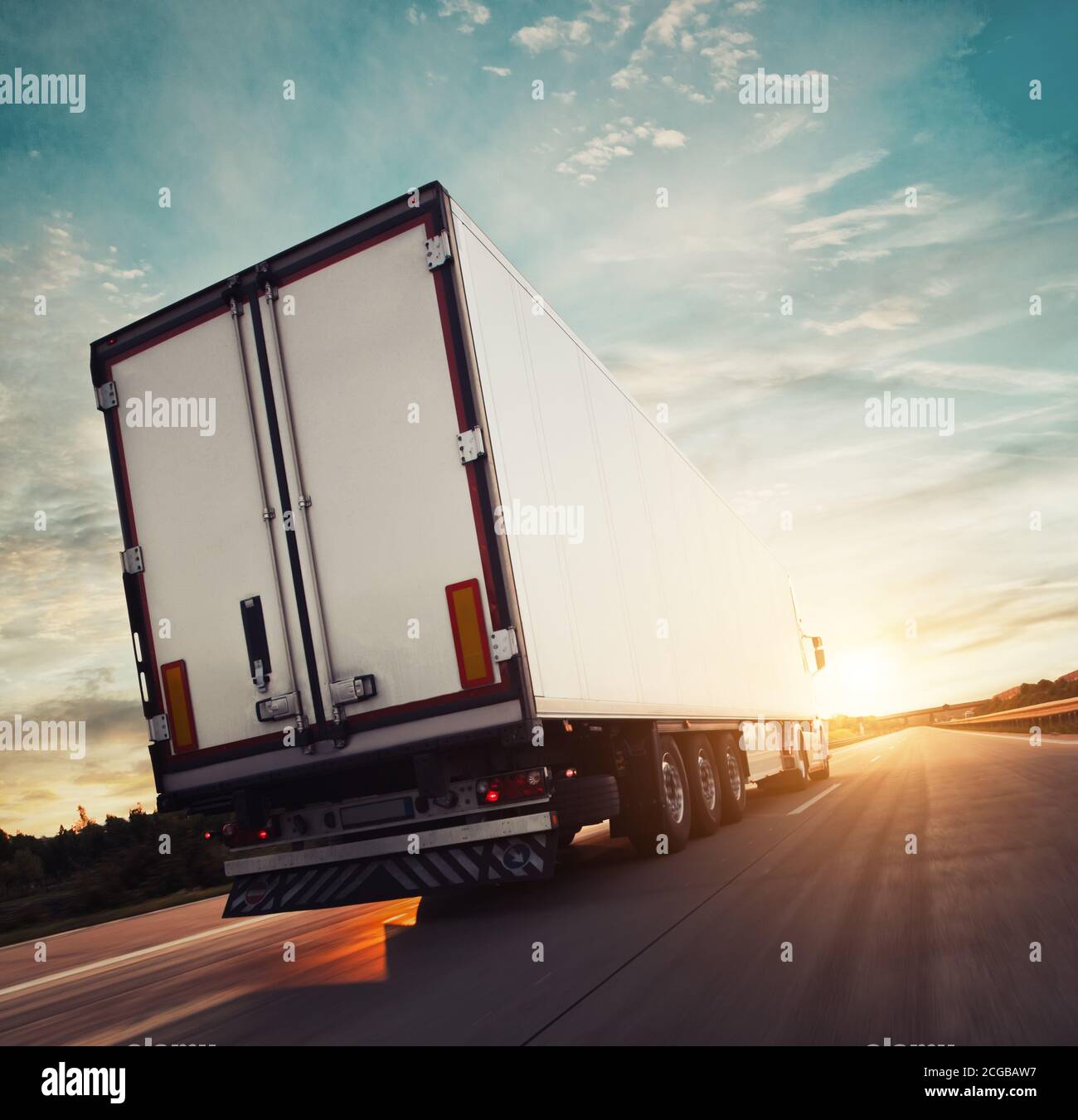 Vue arrière d'un camion européen sur autoroute avec lumière spectaculaire au coucher du soleil. Thème du transport de marchandises et de l'approvisionnement. Banque D'Images