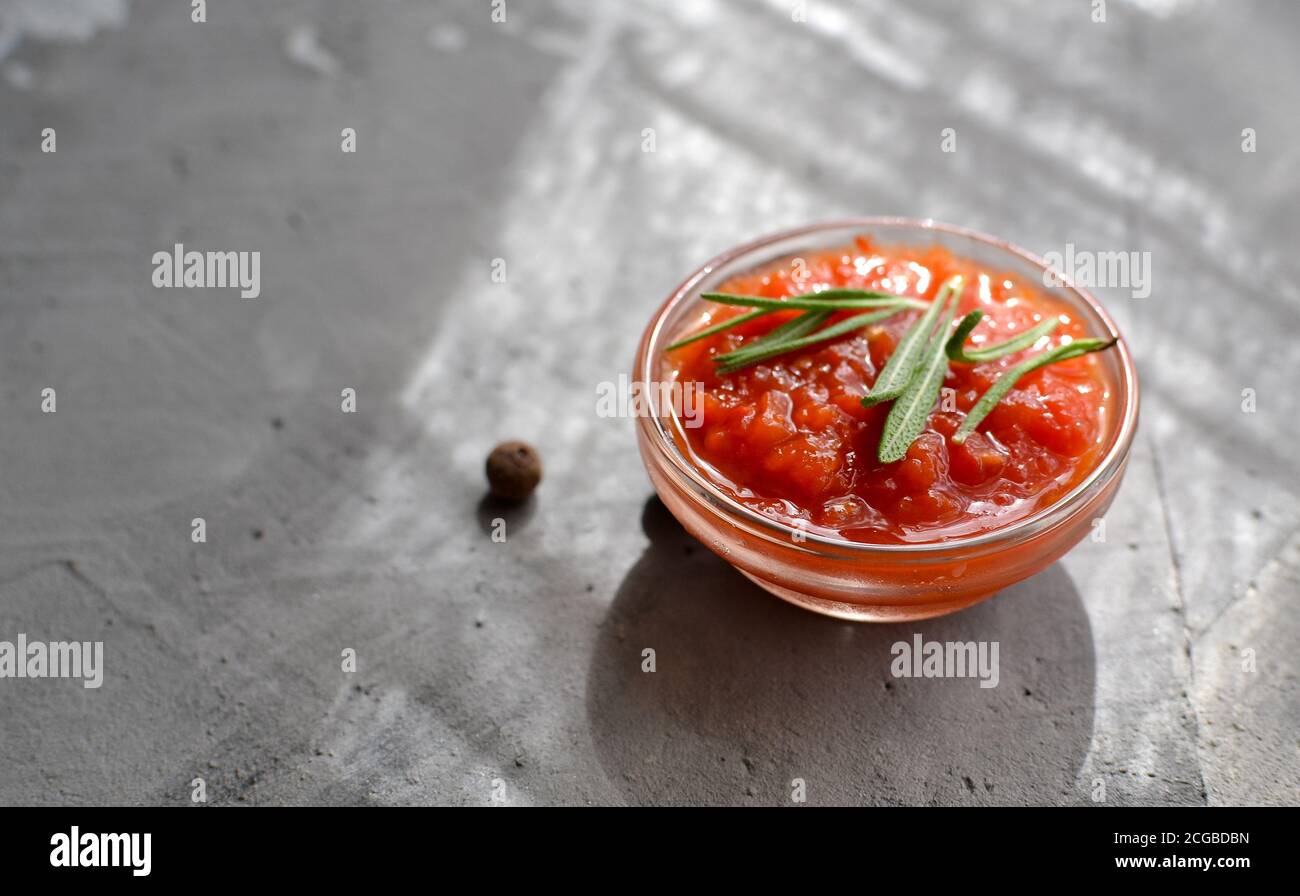 Ketchup dans un bol en verre. Arrière-plan gris. Sauce tomate au romarin. Espace libre pour le texte. Banque D'Images