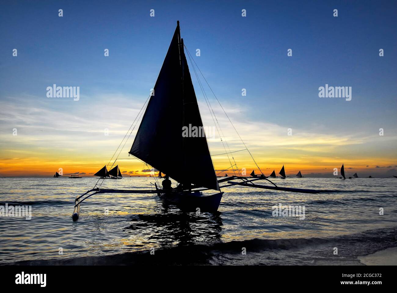 Vue panoramique des voiliers silhouette pour les touristes le long de la plage blanche et à l'horizon au coucher du soleil sur l'île Boracay, Philippines, Asie Banque D'Images