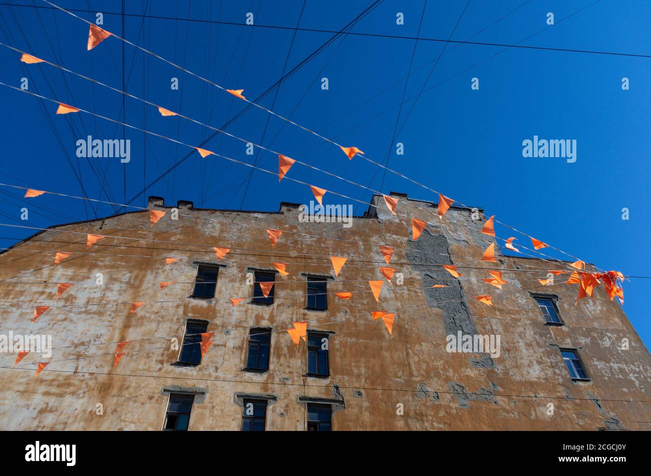 Les drapeaux de fête sont étirés sur les cordes à l'arrière-plan de la maison brune inhabitée et du ciel bleu Banque D'Images