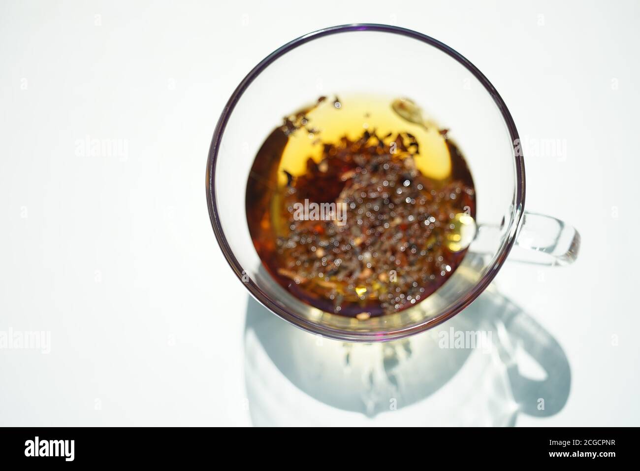 Tasse en verre transparent avec thé floral noir. Vue de dessus sur une table blanche ensoleillée avec ombre. Banque D'Images