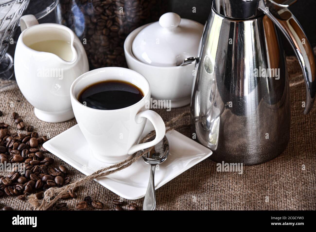 une tasse de café avec des plats blancs, un pot à lait et une sucrière  servis sur une texture jute avec une cafetière thermos argentée Photo Stock  - Alamy