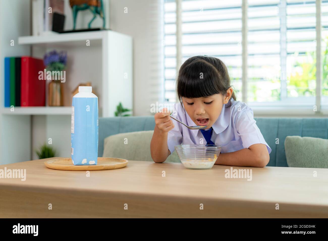 École primaire asiatique fille dans l'uniforme manger des céréales de petit déjeuner avec le lait dans la routine d'école de matin pour la journée dans la vie se préparer à l'école. Banque D'Images