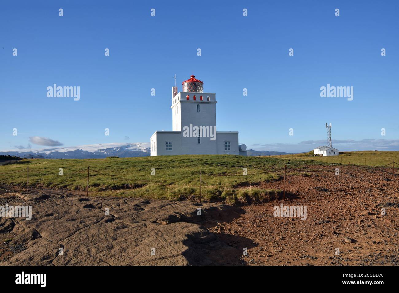 Le phare de Dyrhólaey le long de la côte sud de l'Islande. Une clôture en corde protège l'herbe environnante. Un ciel bleu clair entoure le phare. Banque D'Images