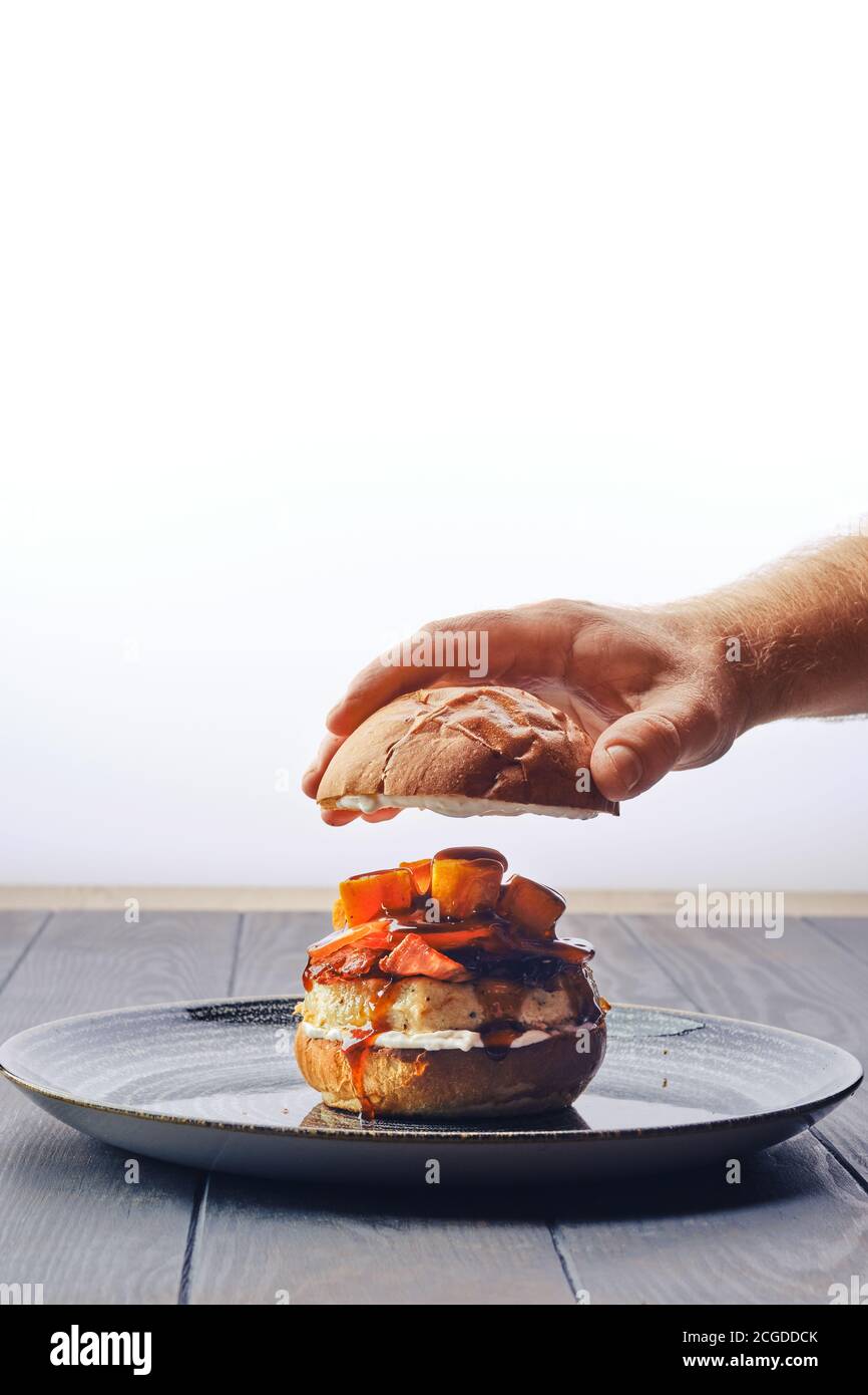 Faire du hamburger avec du bœuf, du bacon, de la citrouille et de la tomate - main masculine met le pain sur le dessus Banque D'Images