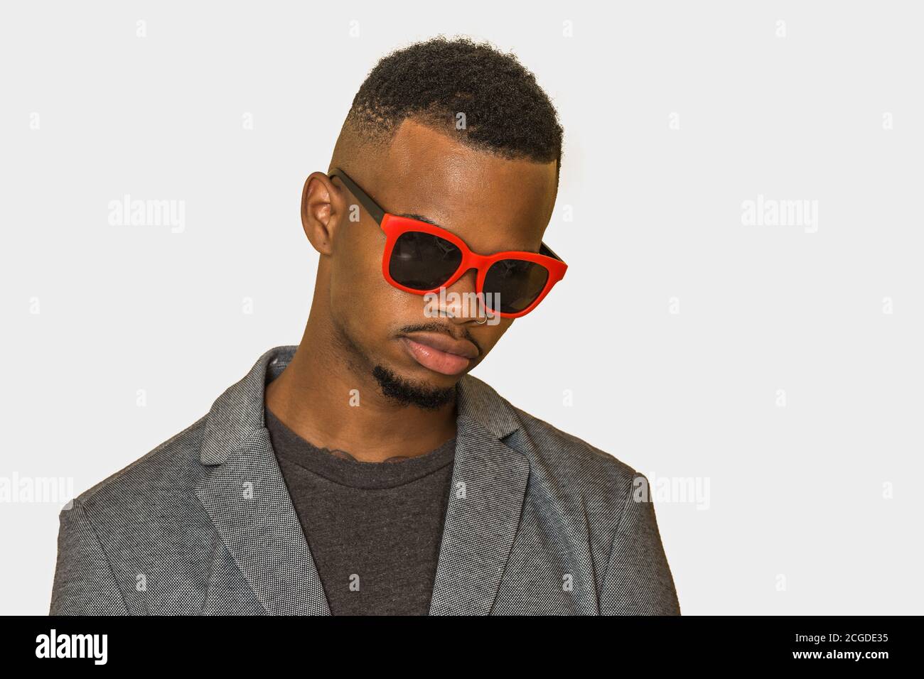 Homme afro-américain en vêtements et lunettes de soleil élégants et décontractés regarder vers le bas sur fond gris Banque D'Images