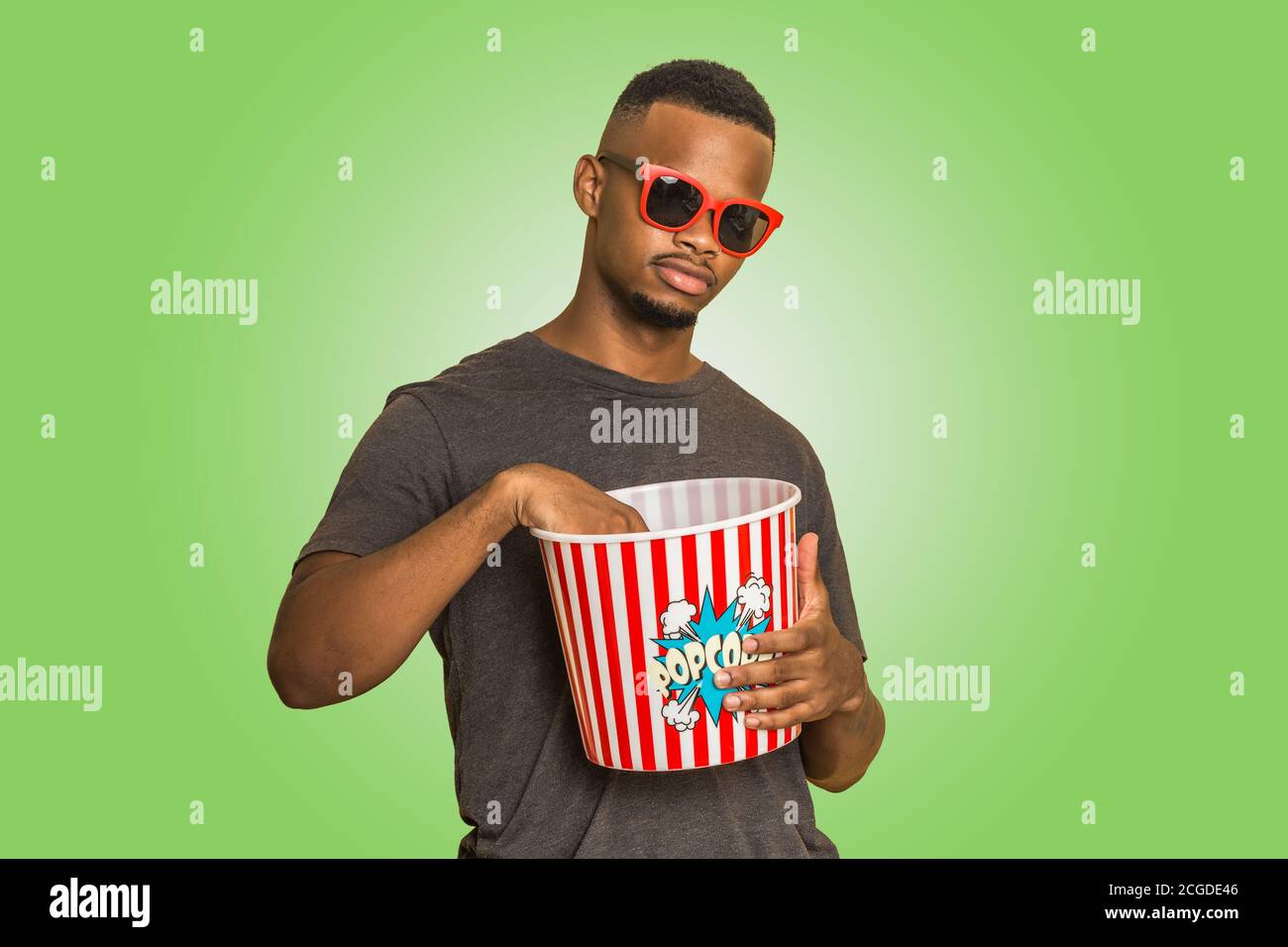 Jeune Afro-américain dans des lunettes de soleil tendance manger du pop-corn de en se tenant sur fond vert Banque D'Images
