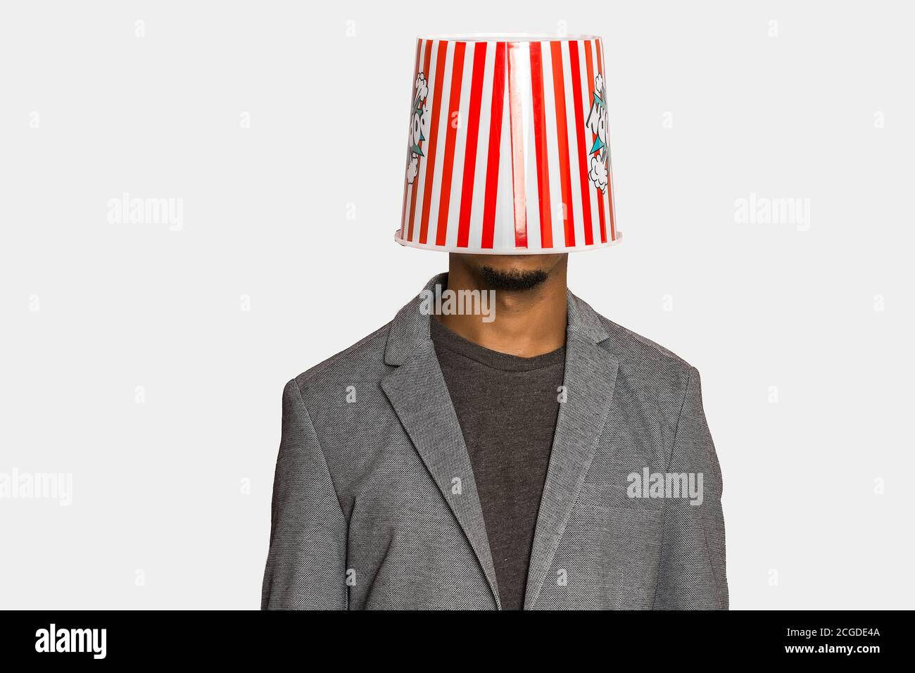 Anonyme ethnique mâle dans des vêtements élégants et décontractés portant du pop-corn à rayures godet sur tête sur fond gris Banque D'Images