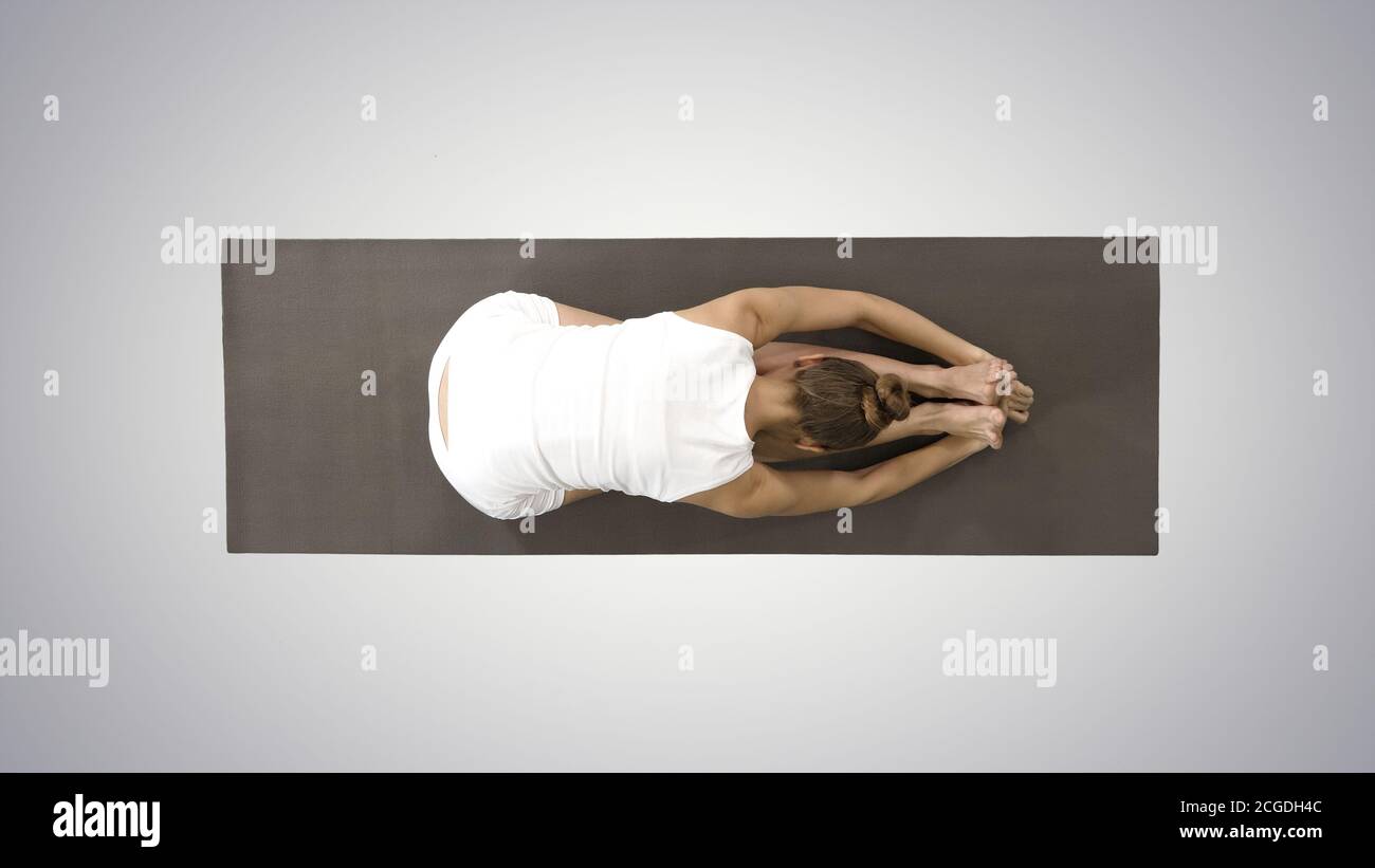 Jeune blonde attrayante femme pratiquant le yoga, faisant un exercice assis de virage vers l'avant, paschimottanasana pose sur fond dégradé. Banque D'Images