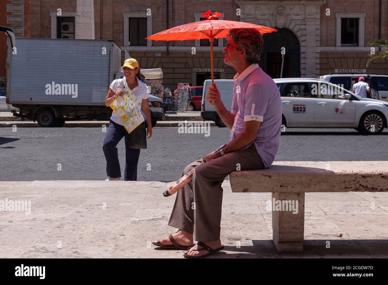 Rome, Italie - 28 juin 2010 : un vendeur de parasols de rue reste assis sur un banc, à côté d'une femme qui travaille comme guide touristique à Rome. Banque D'Images