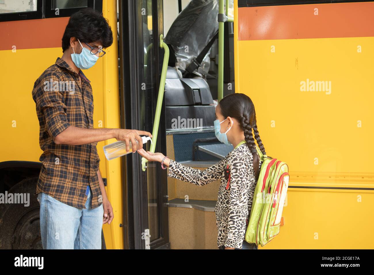 Professeur fournissant de l'assainisseur pour les mains aux élèves avant d'aller ou d'obtenir à l'intérieur de l'autobus scolaire tout en maintenant la distance sociale comme coronavirus ou covid Banque D'Images