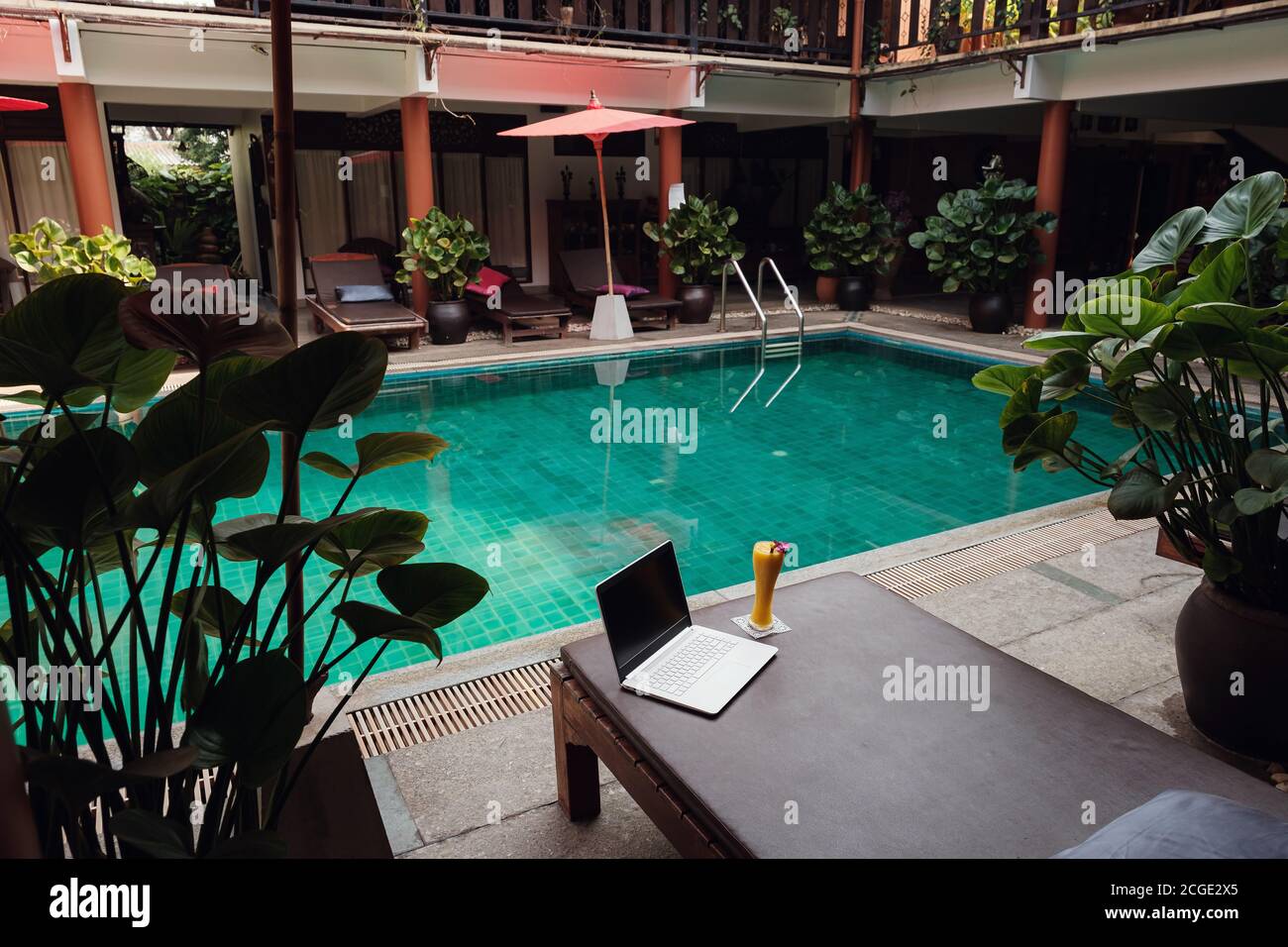 Un ordinateur portable blanc, un smartphone et un smoothie à la mangue sur un lit de soleil sur fond de piscine. Un début de journée. Concept d'entreprise freelance. Flexible RE Banque D'Images