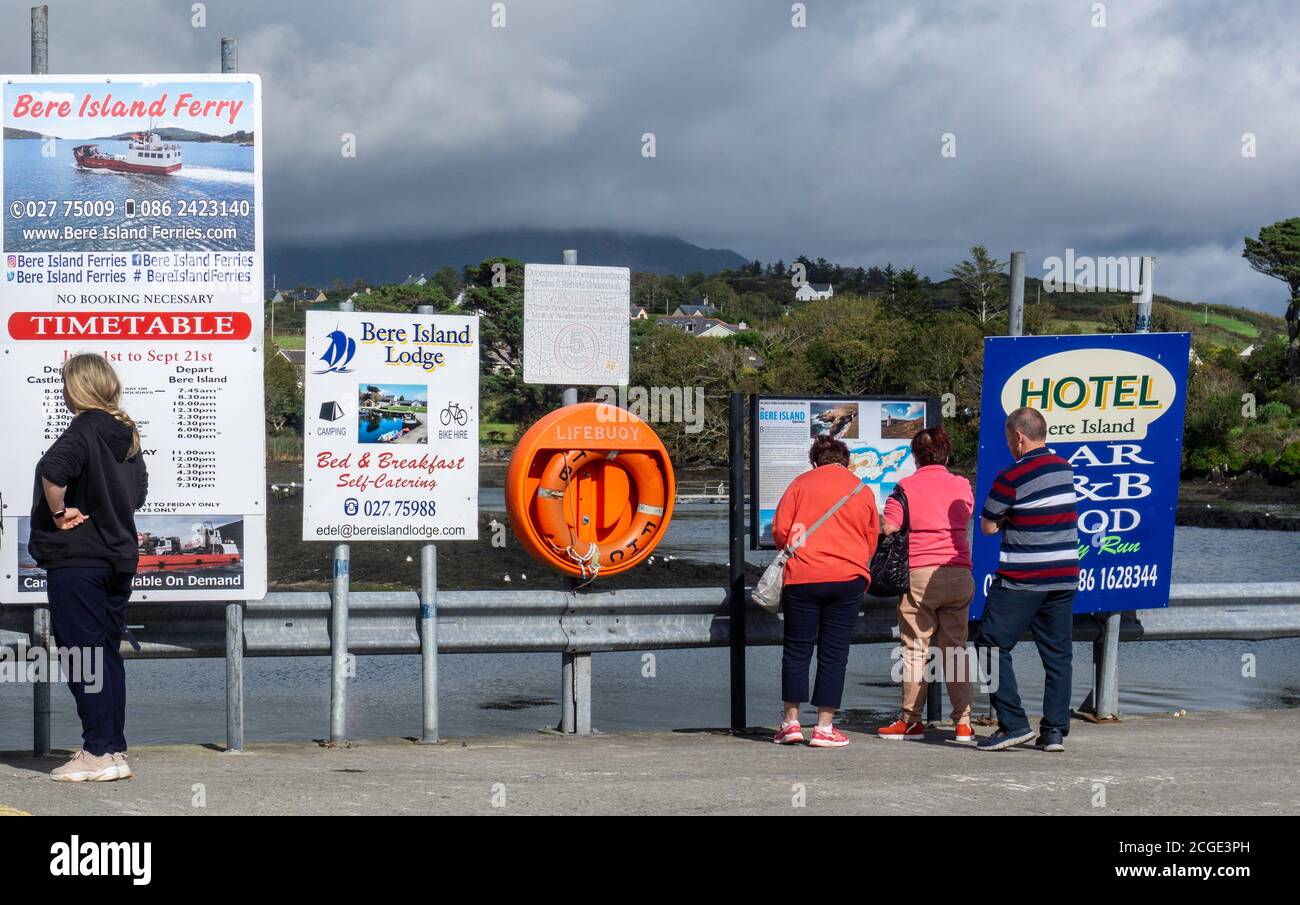 Une femme inspectant l'horaire du ferry de l'île de Bere à Castletownbere, comté de Cork en Irlande, comme d'autres vérifient une affiche pour l'île de Bere. Banque D'Images