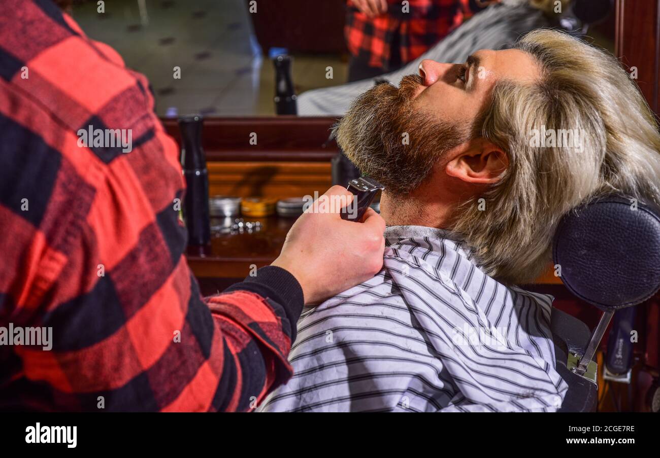 Barbu et élégant. homme de taille basse avec barbe coupant ses cheveux dans un barbershop. Coiffeur professionnel. Style de vie. Master barber fait la coiffure et le coiffage avec le sèche-cheveux. Concept Barbershop. Banque D'Images