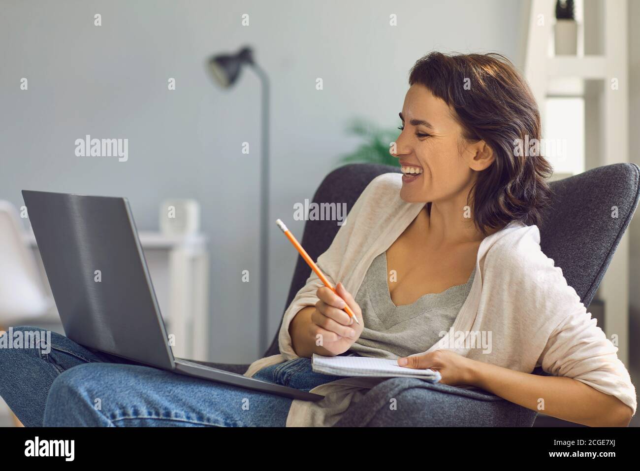 Femme souriante assise avec un ordinateur portable et prenant des notes en ligne réunion Banque D'Images