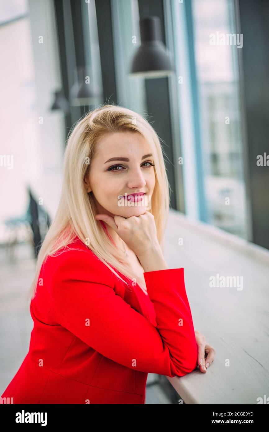 Belle femme d'affaires réussie dans un costume rouge dans un bâtiment de bureau léger près de la fenêtre Banque D'Images