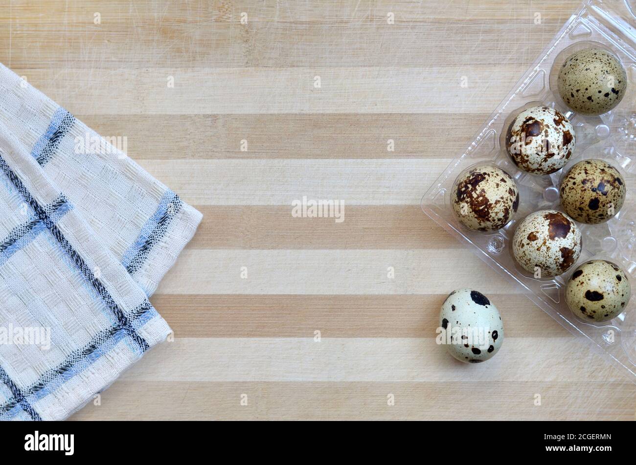 Œufs de caille mouchetés dans un plateau en plastique transparent sur une planche à découper en bois avec une serviette de cuisine en gros plan avec espace de copie, vue du dessus. Une alimentation saine Banque D'Images