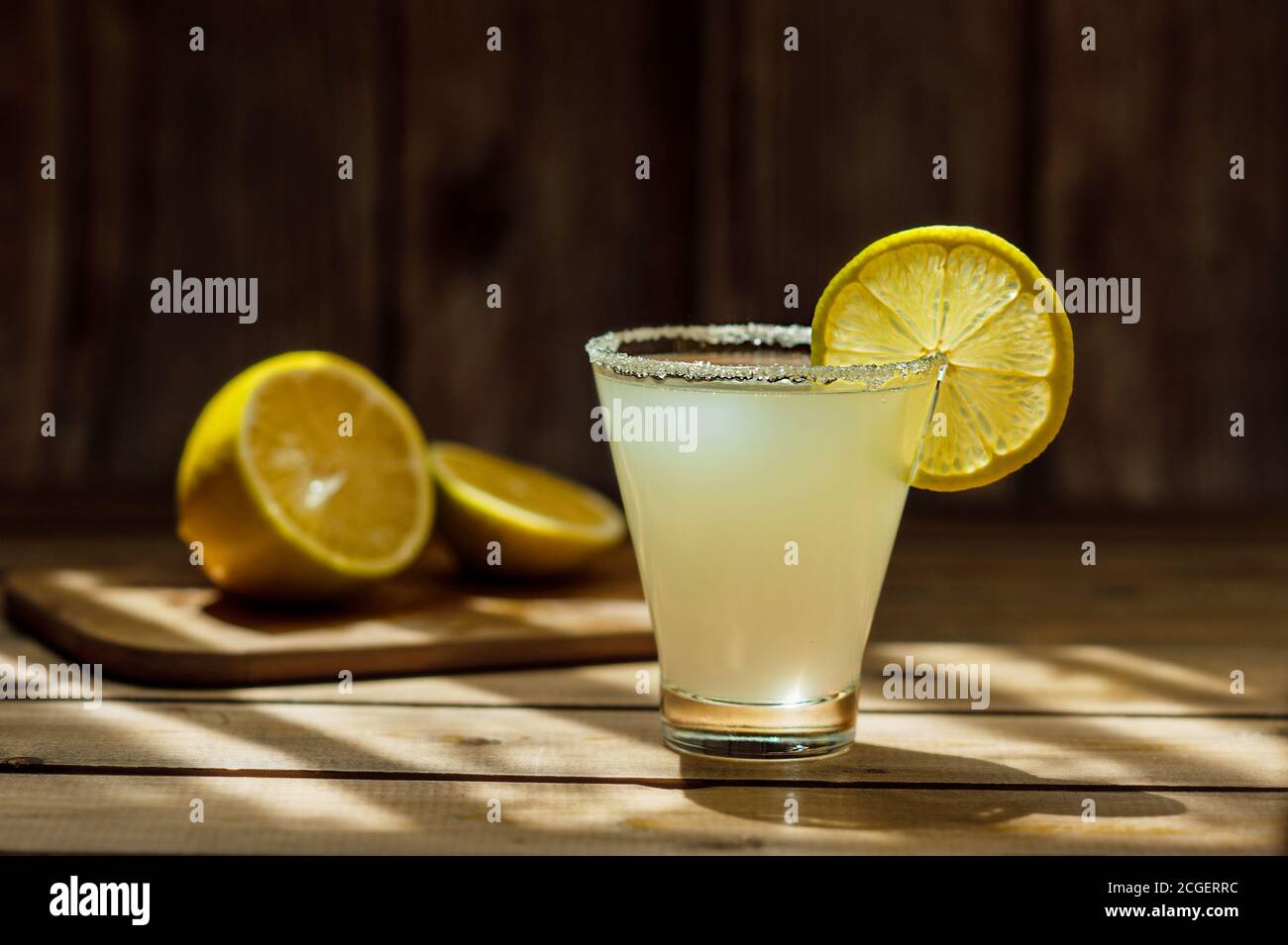 boisson alcoolisée jaune d'été dépolie dans un verre de forme transparente avec du sucre sur le rebord et un juteux mûr rond tranche de citron sur une table en bois et Banque D'Images