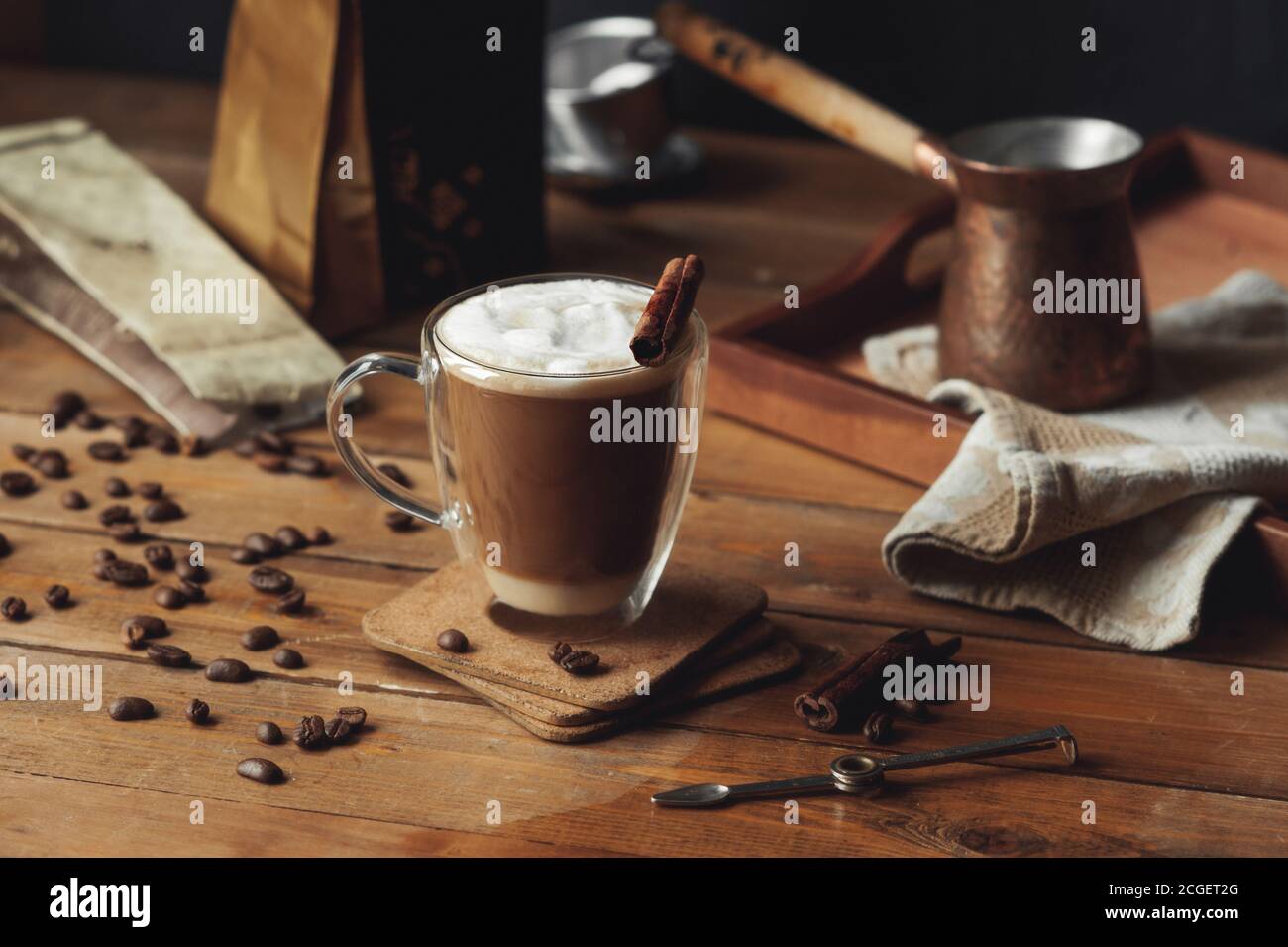 Tasse à café en verre transparent avec parois doubles et café versé en couches avec de la cannelle et de la mousse de lait sur du bois rugueux table et café dispersé bea Banque D'Images