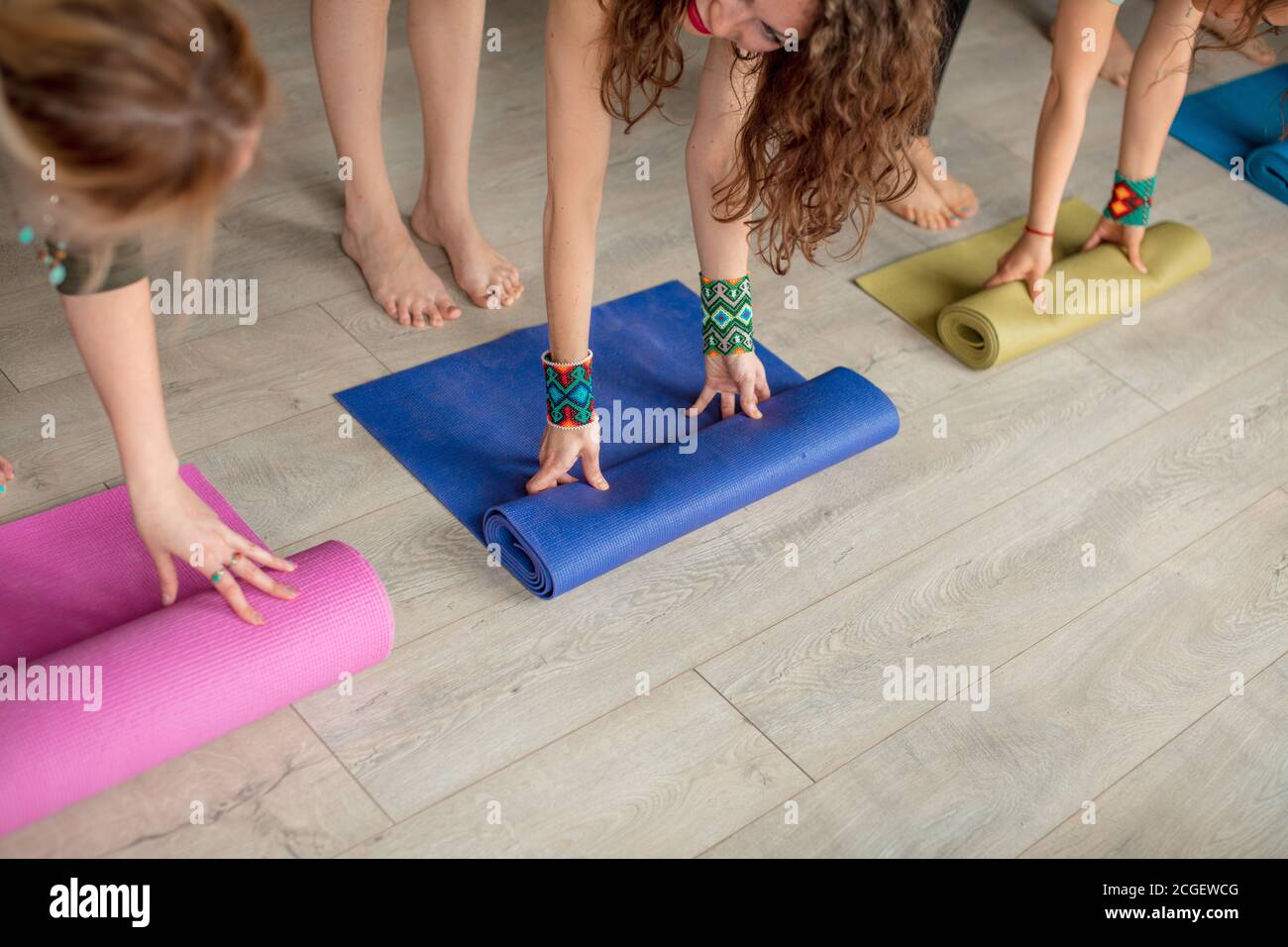 Vue rognée des mains des femmes déroulant des tapis de yoga colorés avant de pratiquer le yoga, en préparant pour l'exercice dans l'intérieur du studio Banque D'Images