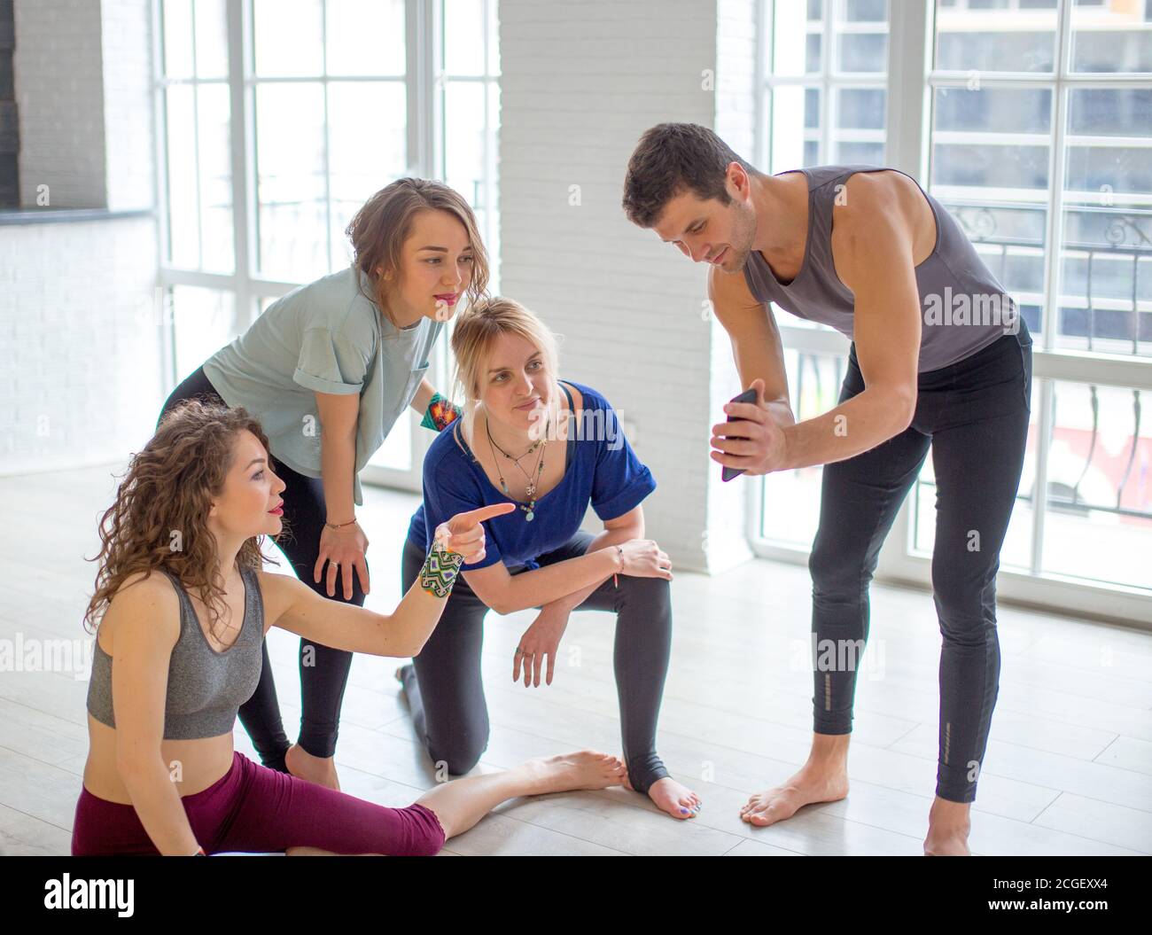 Homme en tenue de yoga partageant des photos avec ses gymnases féminins, en  utilisant un smartphone, tout en étant assis sur le sol d'une salle de gym  avant de pilates entraînement Photo