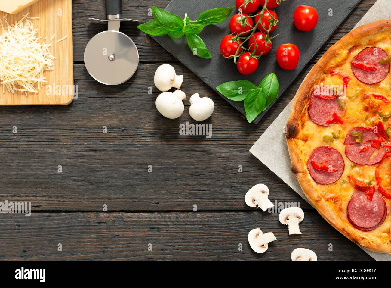 Savoureuse pizza chaude avec des ingrédients et un couteau à pizza sur fond de texture noire. Vue de dessus Banque D'Images