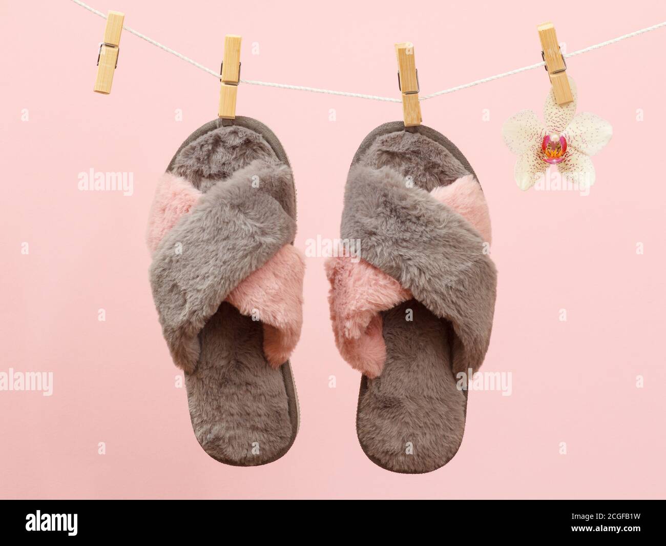 Chaussons doux bruns pour femmes sur une corde à linge avec des épingles à linge et une fleur d'orchidée sur fond rose. Banque D'Images