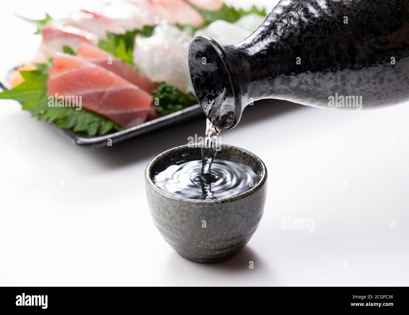 Le saké est versé dans une tasse de saké fixée sur un fond blanc. Sashimi à l'arrière. Banque D'Images