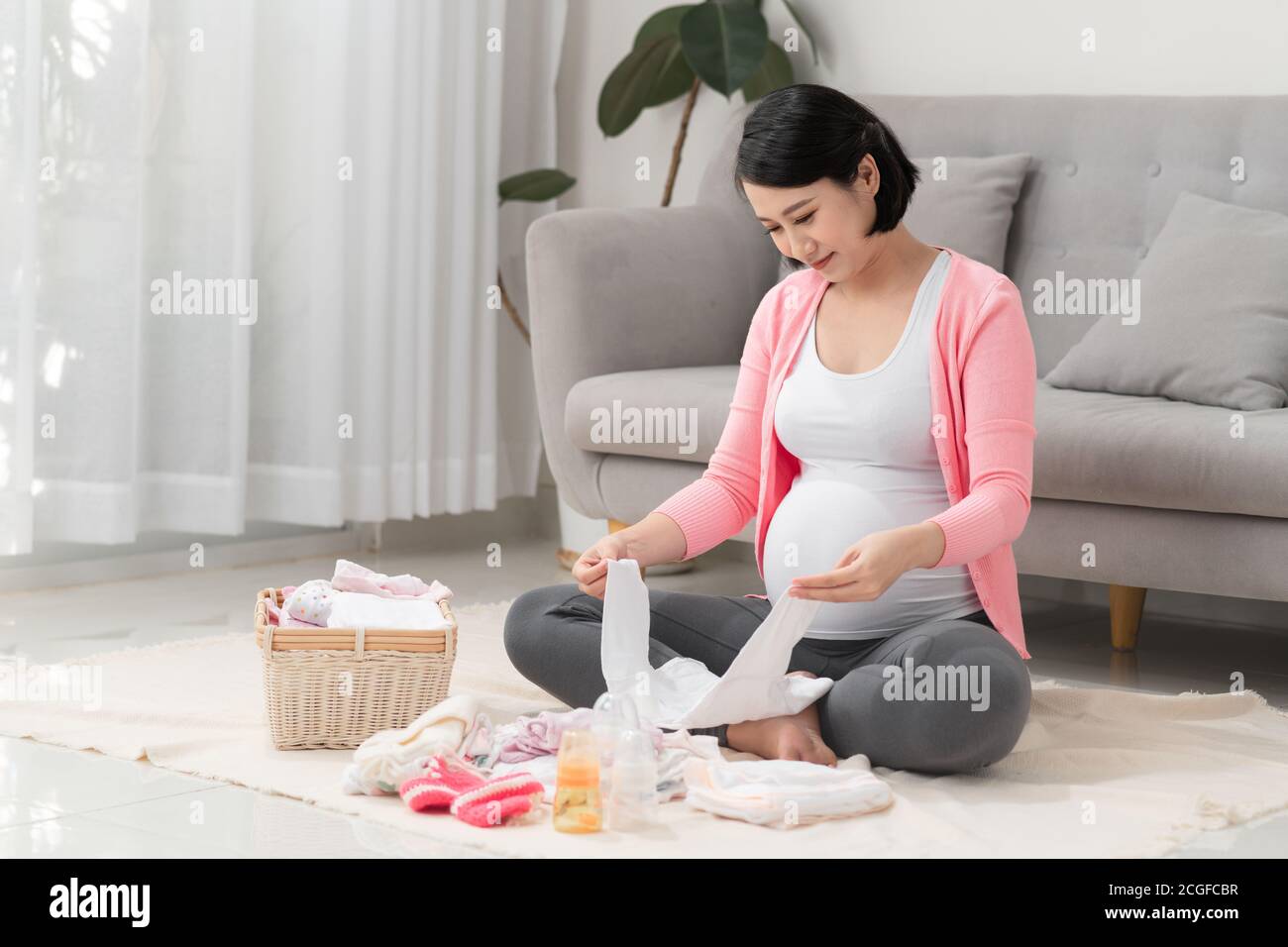 belle femme asiatique enceinte utilisant la liste d'écriture de stylo sur le bloc-notes emballage et préparation des vêtements de bébé dans le panier Banque D'Images