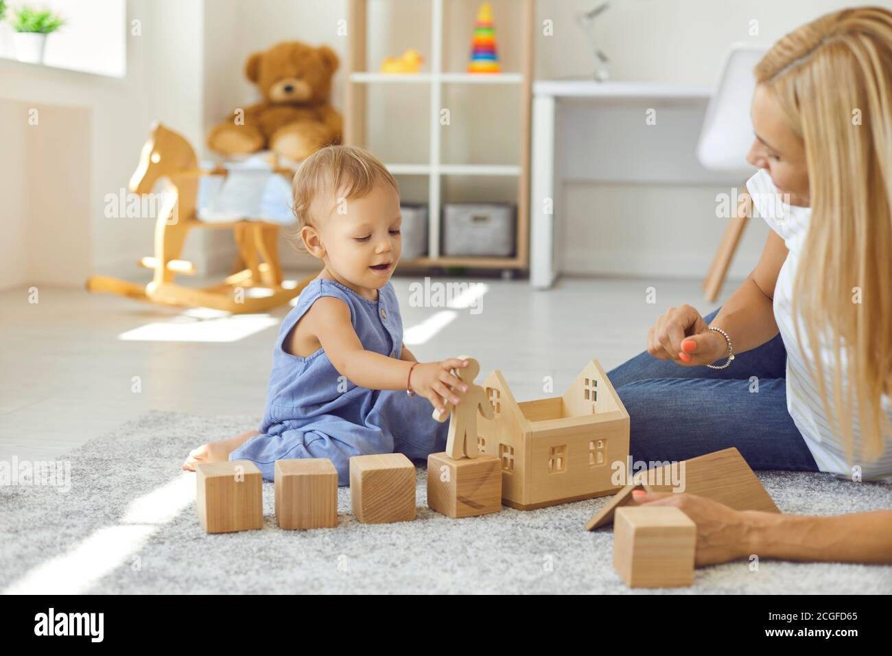 Joyeux baby-sitter et petit enfant jouant avec des blocs de bois dans une chambre confortable Banque D'Images