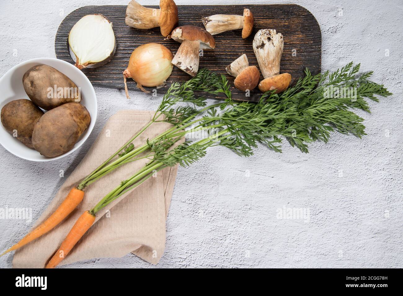 Ingrédients pour cuire divers plats de champignons porcini de forêt sur un fond léger - champignons, carottes, pommes de terre, oignons, avec une coupe en bois Banque D'Images