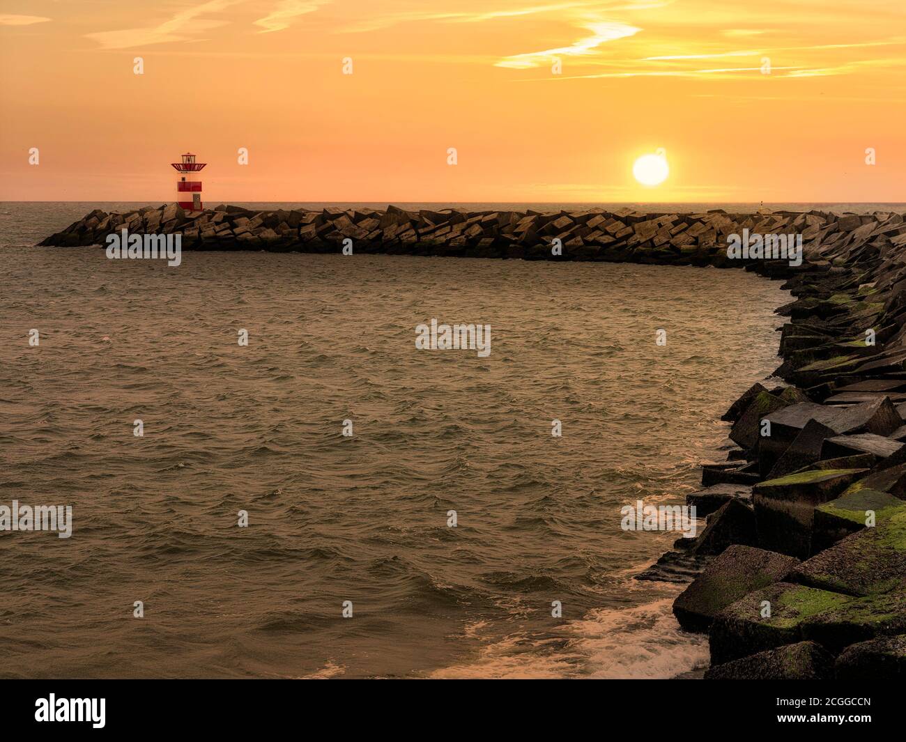 Coucher de soleil sur l'entrée du sémaphore rouge du canal du port construit avec des blocs de béton cubes Banque D'Images