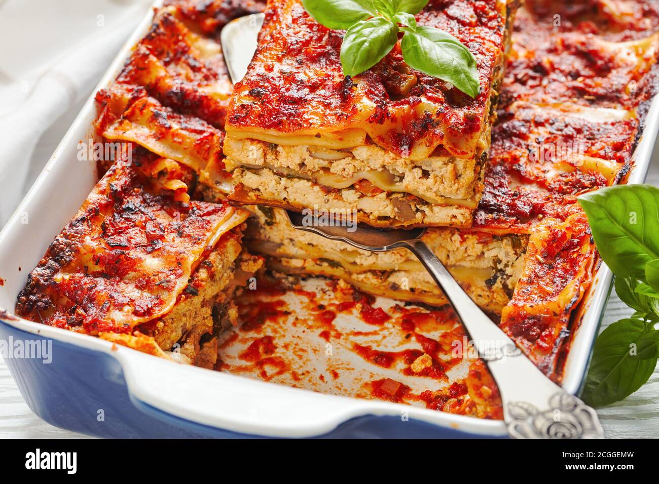 Lasagnes de tofu à faible teneur en matières grasses végétaliennes aux champignons champignons, sauce tomate, assaisonnement italien, servies sur un plat de cuisson aux herbes fraîches, sur un tabl en bois blanc Banque D'Images