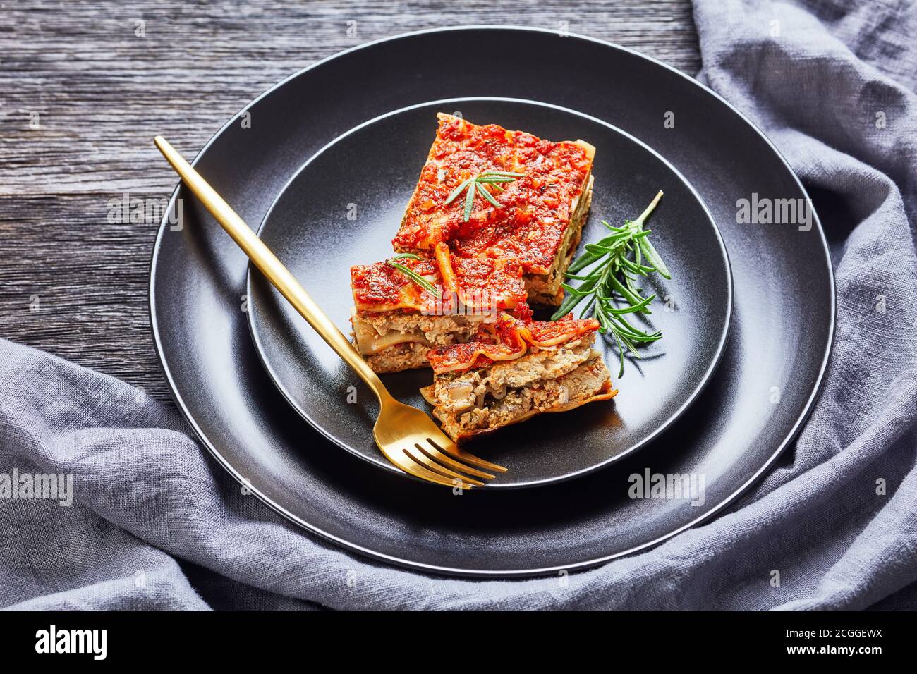 Lasagnes aux épinards et au tofu vegan au champagne et bolognaise aux tomates Et assaisonnement italien servi sur une assiette noire avec fourchette et romarin frais sur un Banque D'Images
