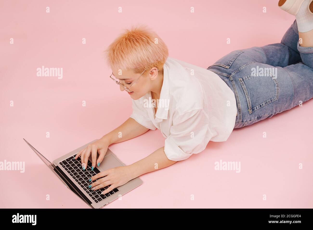 Jeune femme avec des cheveux courts couché sur le ventre sur le sol, travaillant sur un ordinateur portable Banque D'Images