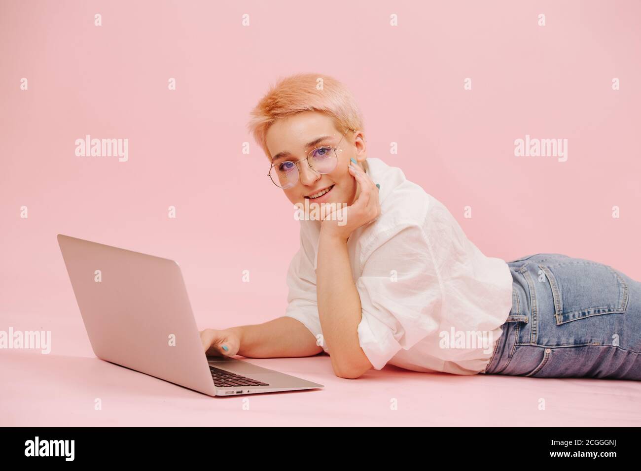 Une femme heureuse avec des cheveux courts couchés au ventre sur le sol, travaillant sur un ordinateur portable Banque D'Images