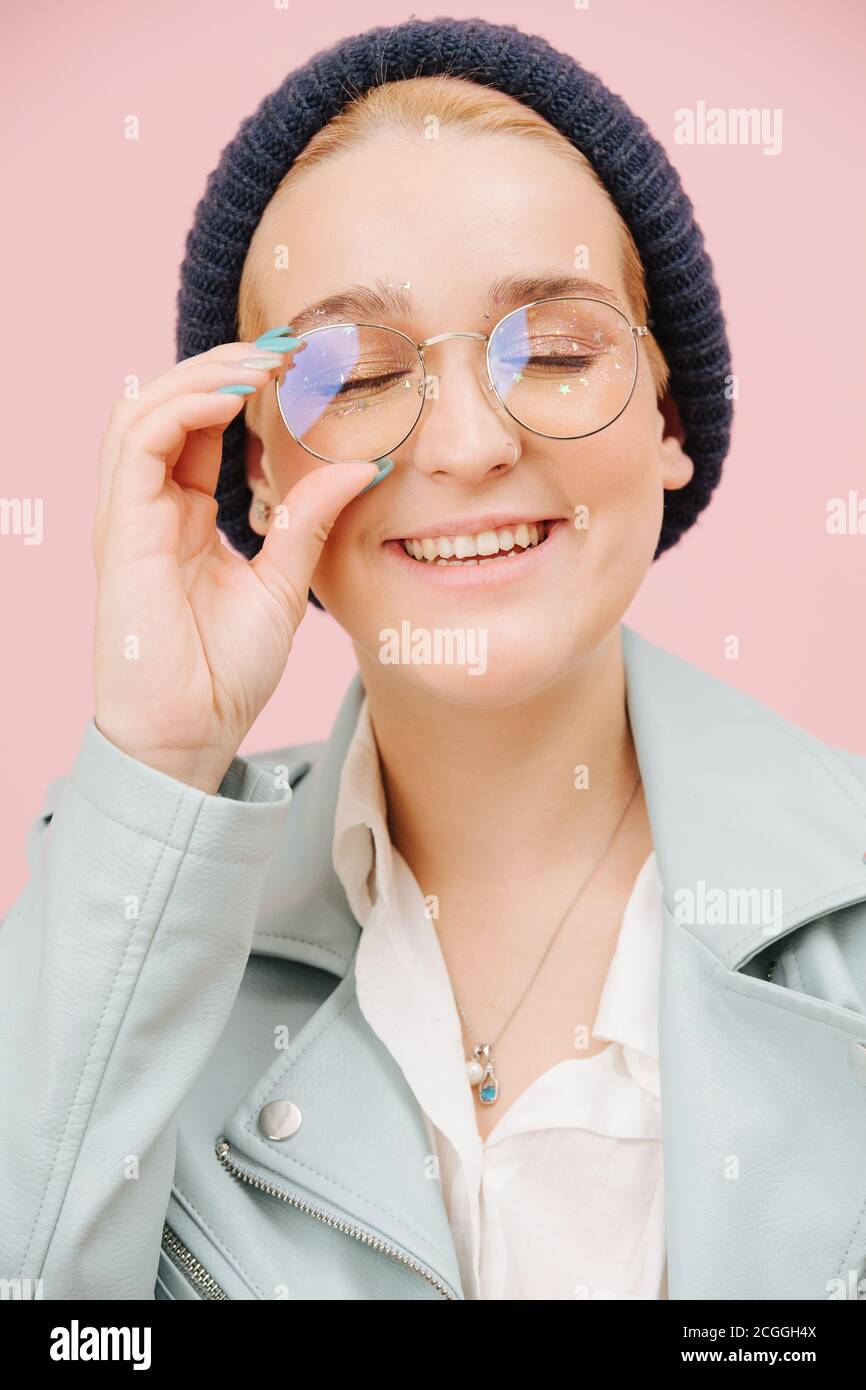 Joyeux rire jeune femme dans un chapeau et des verres ronds souriant avec les yeux fermés. Banque D'Images