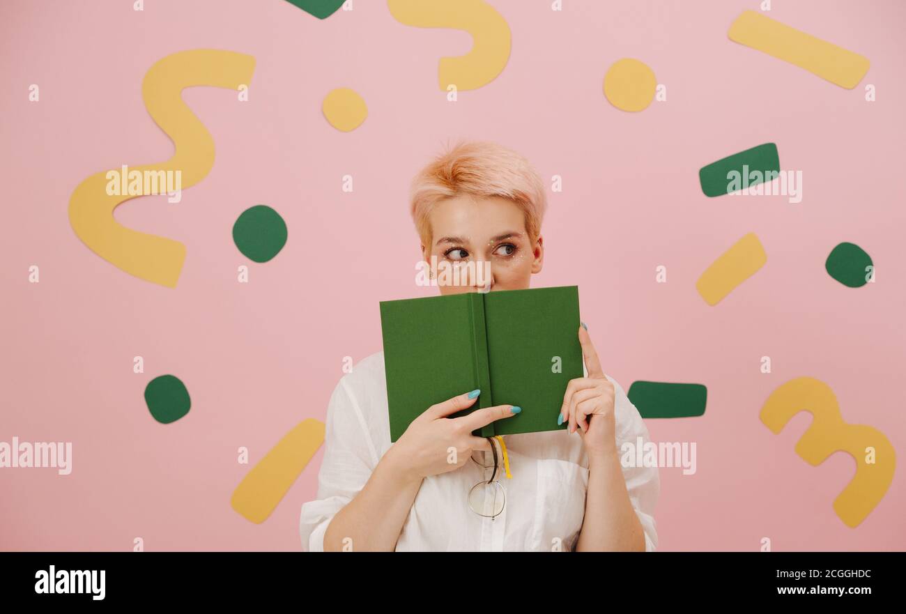 Jeune femme prudente avec des cheveux blonds courts couvrant sa bouche avec un livre Banque D'Images