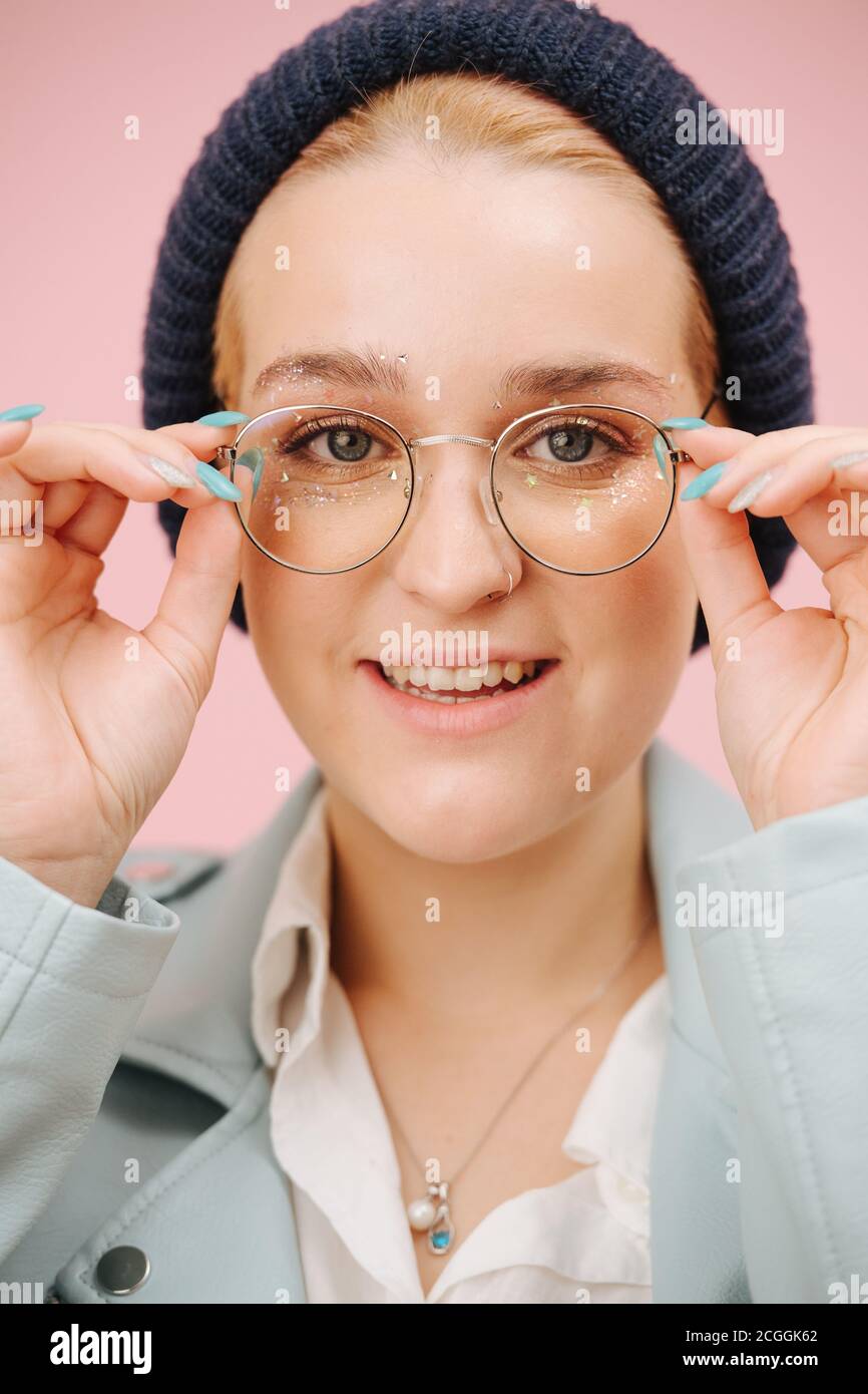 Jeune femme excentrique enthousiaste dans une casquette et des verres ronds. Sur rose. Banque D'Images