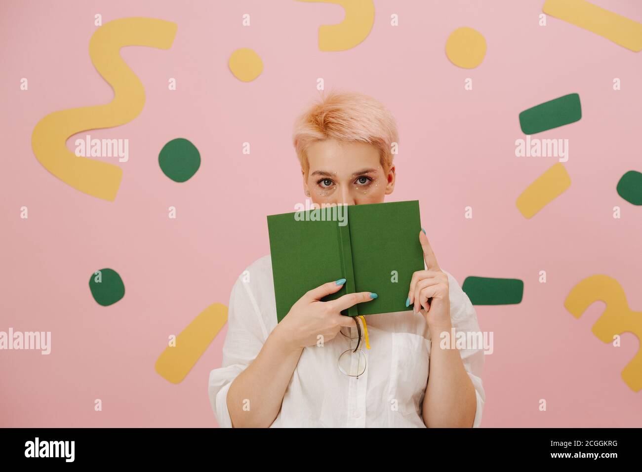 Jeune femme timide aux cheveux blonds courts recouvrant sa bouche avec un livre Banque D'Images