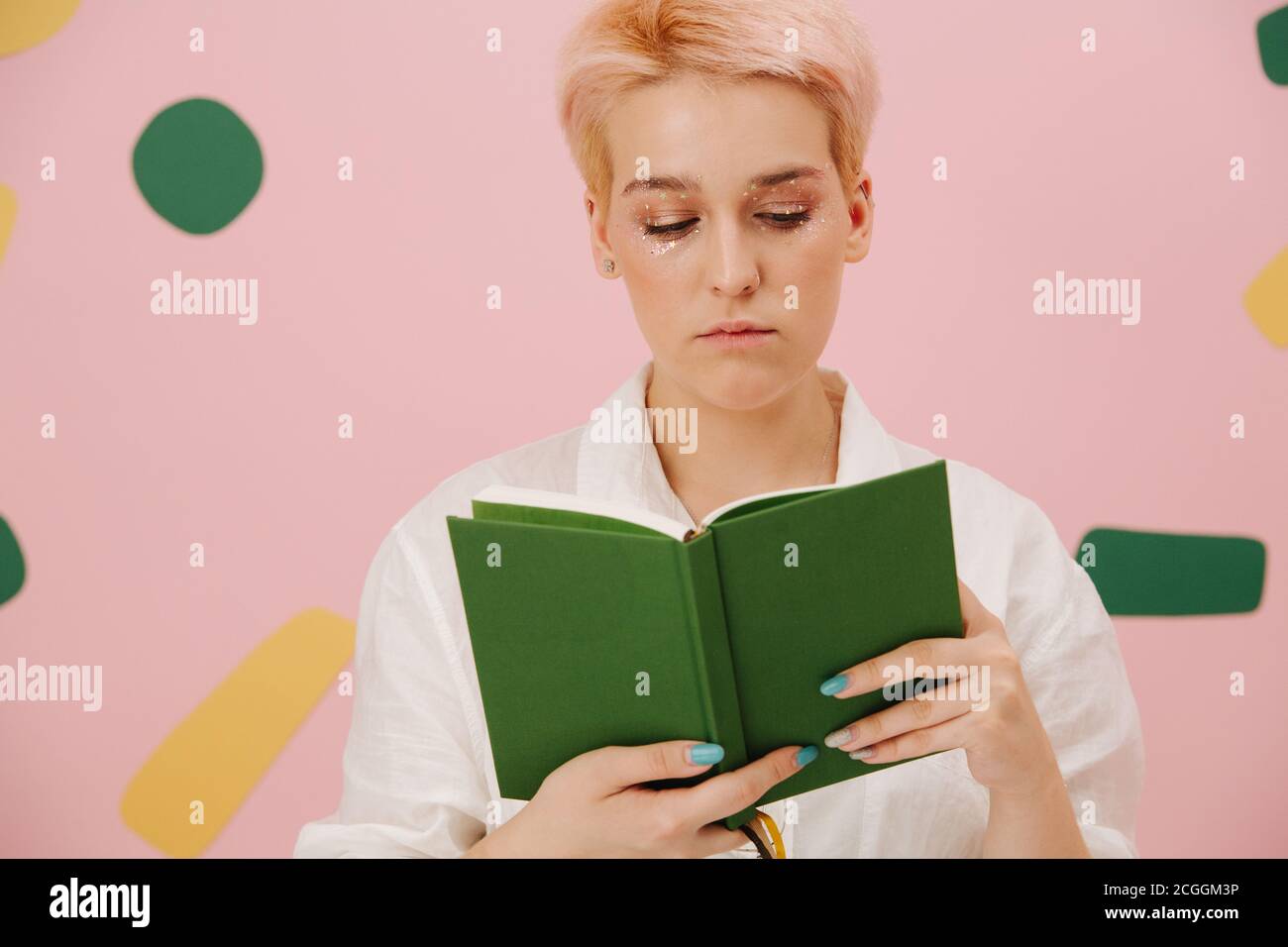 Jeune femme vif avec un livre de lecture de cheveux blond court. Sur rose. Banque D'Images