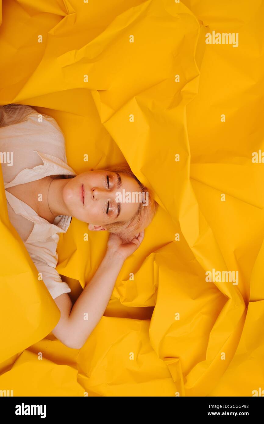 Jeune femme heureuse avec des cheveux courts couchés sur le dos sur papier jaune étroit Banque D'Images