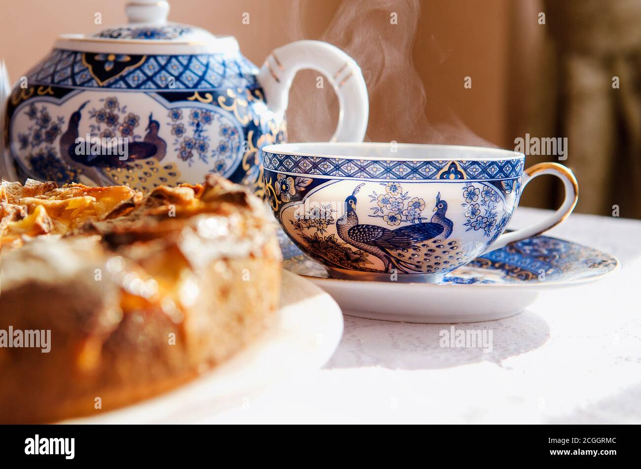 Tarte aux pommes sur un plat blanc, une théière et deux tasses de thé chaud sur une table recouverte d'une nappe blanche. Banque D'Images